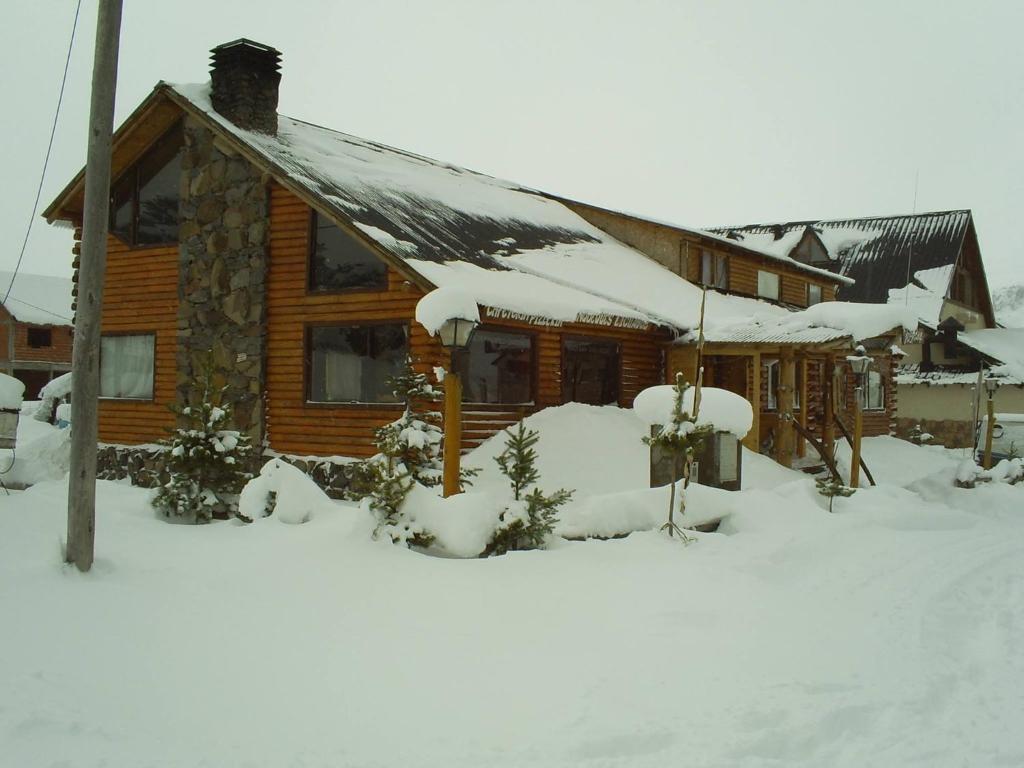 Cabaña de madera con nieve en el techo en Hostería de Montaña los Duendes del Volcán en Caviahue