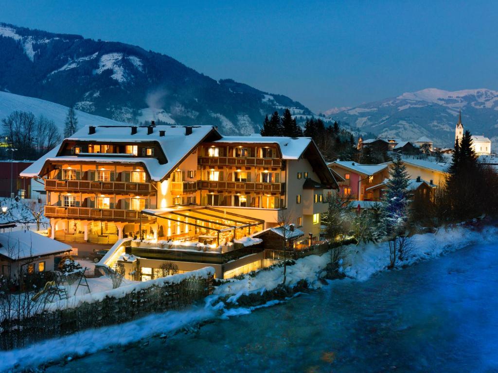 a large building with snow on it next to a river at Hotel Kaprunerhof in Kaprun