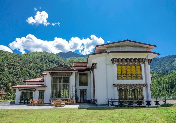 a large white house with mountains in the background at The Postcard Dewa, Thimphu, Bhutan in Thimphu