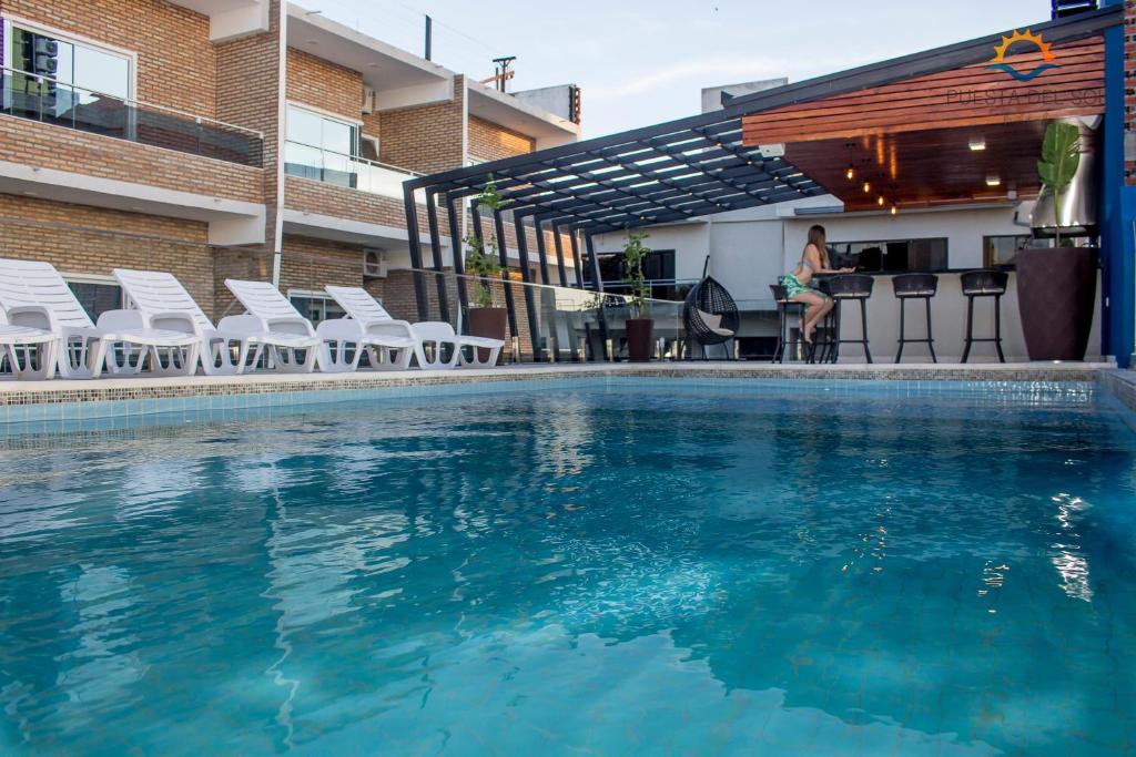 a swimming pool with chairs and a woman sitting at a bar at Hotel Puesta del Sol in Encarnación