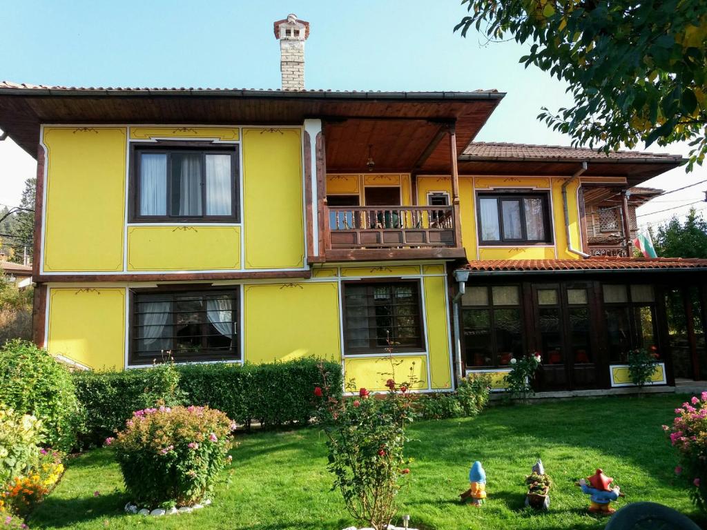 a yellow house with a balcony and a yard at Guest House Bolyarka in Koprivshtitsa