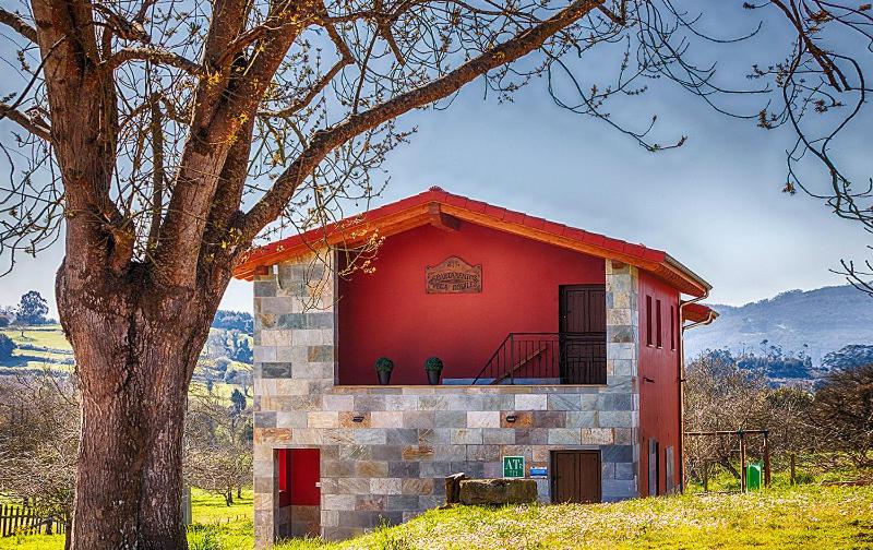 a red building with a tree in front of it at Apartamentos Vega Rodiles la huerta in Villaviciosa