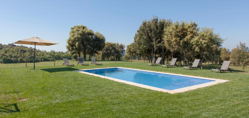a pool in the grass with chairs and an umbrella at El Porxo de Mateus in Sagás