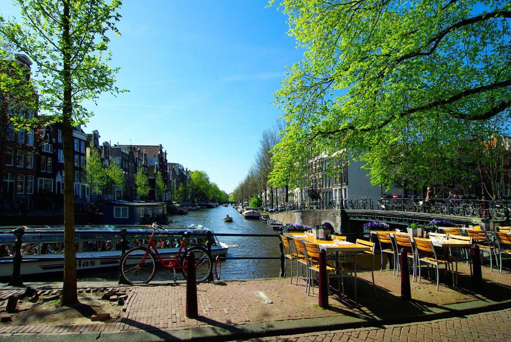 einen Fluss mit Tischen und Stühlen neben einem Kanal mit Booten in der Unterkunft The Mallory in Amsterdam