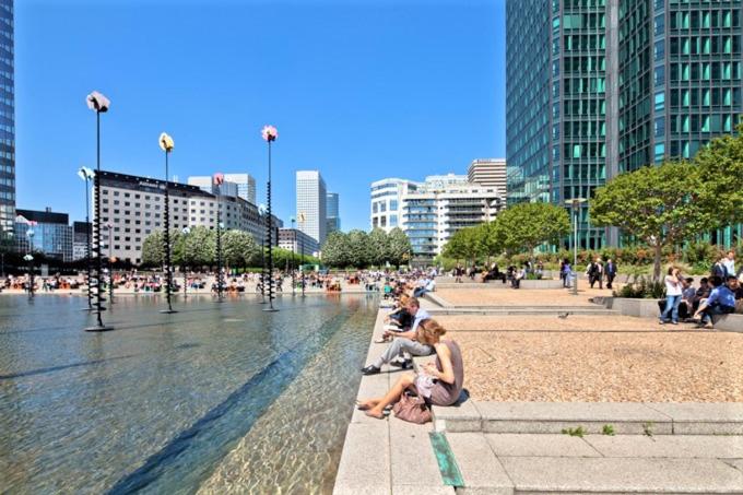a group of people sitting on a bench next to a fountain at Appartement Lilas Parc 1 - Paris La Défense in Courbevoie