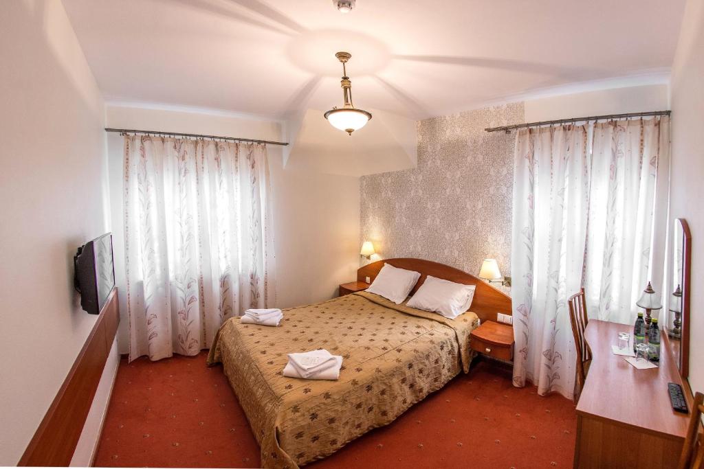 a bedroom with a bed and a desk and curtains at Hotel Karczówka in Kielce