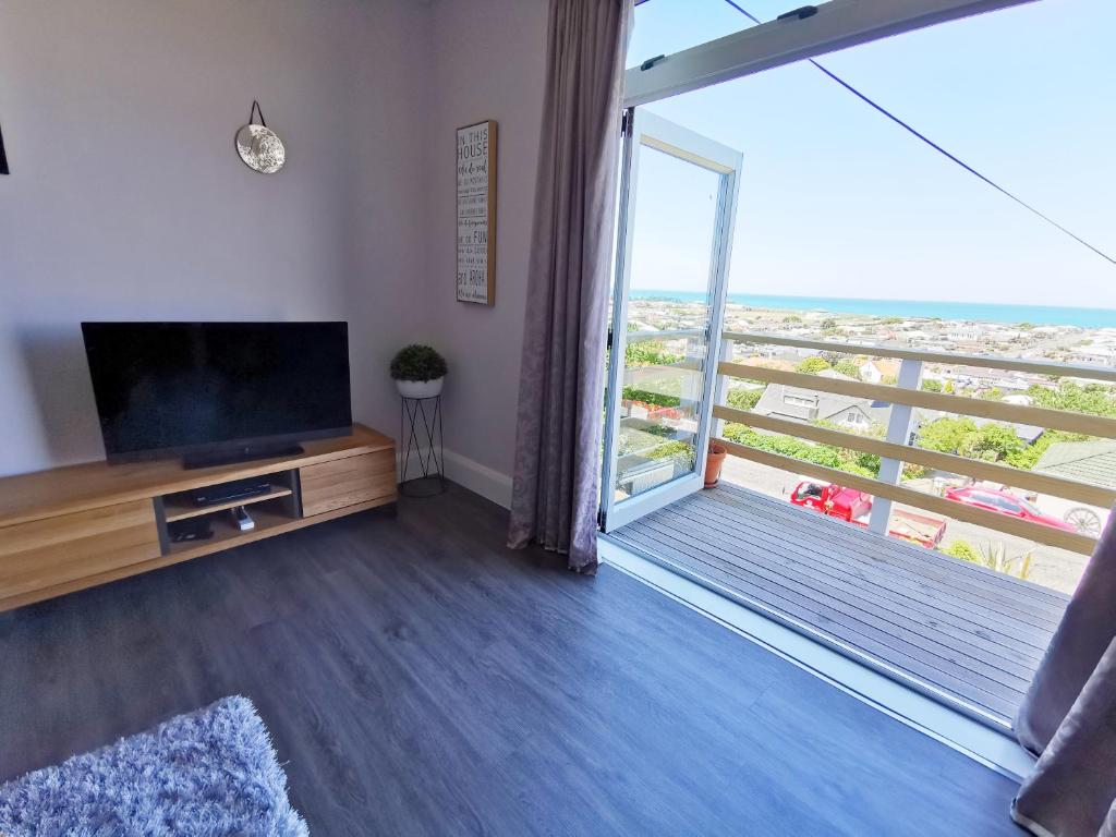 a living room with a flat screen tv and a balcony at 180 degrees sea view 180度全海景房 in Oamaru