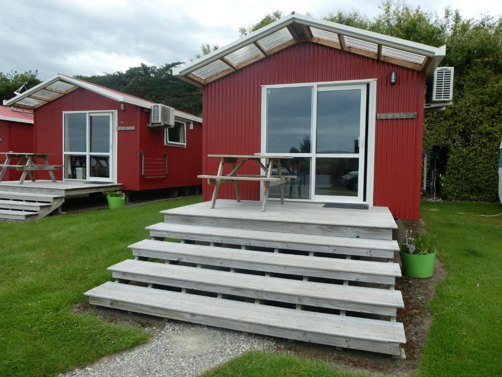 a red cottage with stairs leading to a patio at Motels by the Moeraki Boulders Holiday Park in Hampden