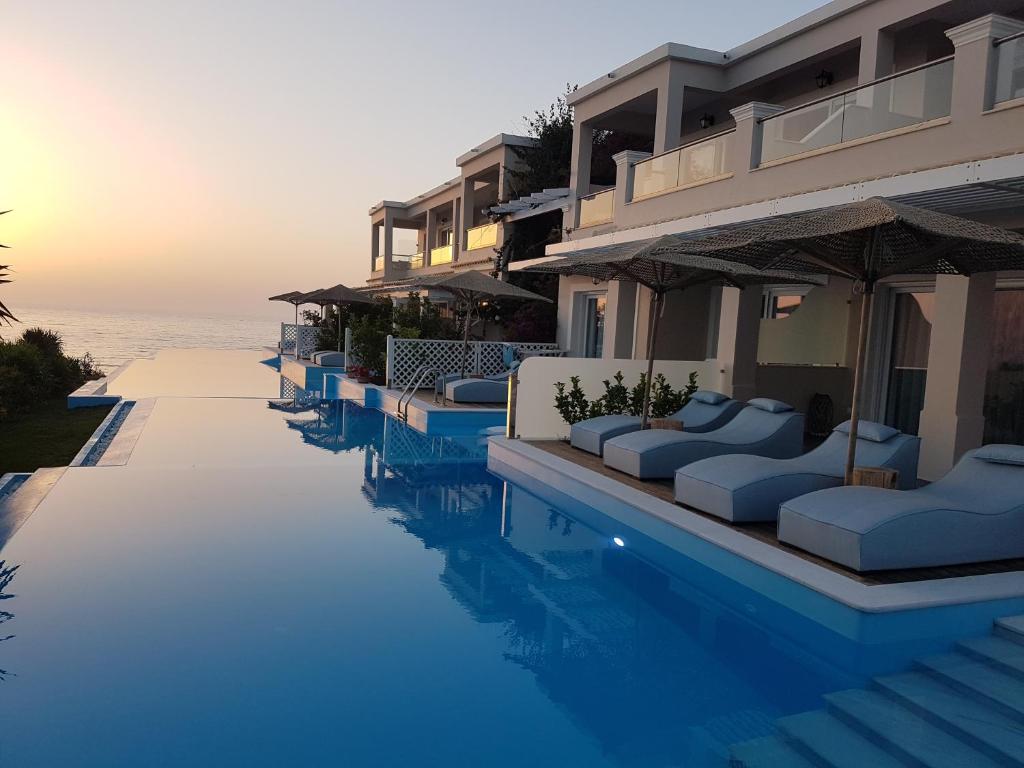 a hotel swimming pool with couches and the ocean at Paralia Luxury Suites in Agios Stefanos