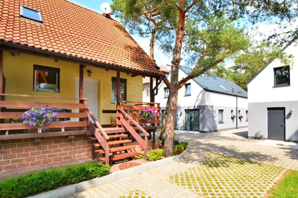 a yellow house with a wooden porch and a tree at Sosnowka in Pobierowo