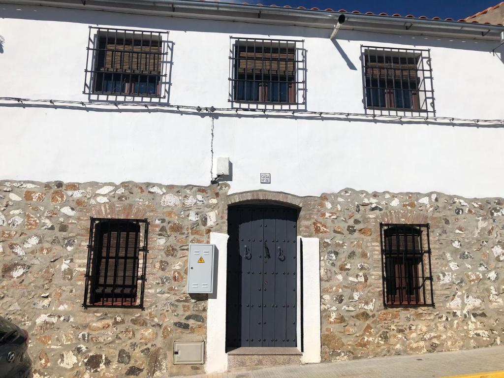 um edifício de pedra com uma porta preta e janelas em Casa La montera em El Alcornocal