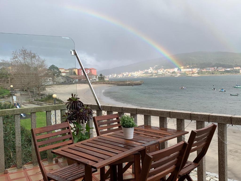 een houten tafel en stoelen op een balkon met een regenboog bij Casa Mar y Sol in Corcubión