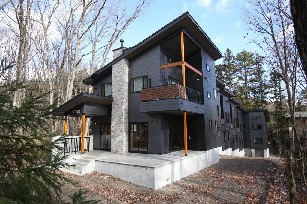 a black house with a balcony in the woods at The Seasons Apartments Hakuba in Hakuba