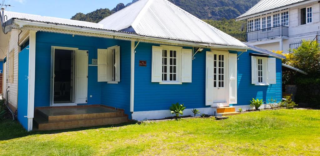 une maison bleue avec une porte blanche dans une cour dans l'établissement Le Cascavelle, à Cilaos