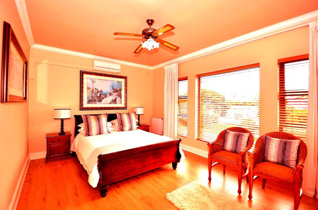 a bedroom with a bed with a ceiling fan and two chairs at Casa Mia Guesthouse in Table View