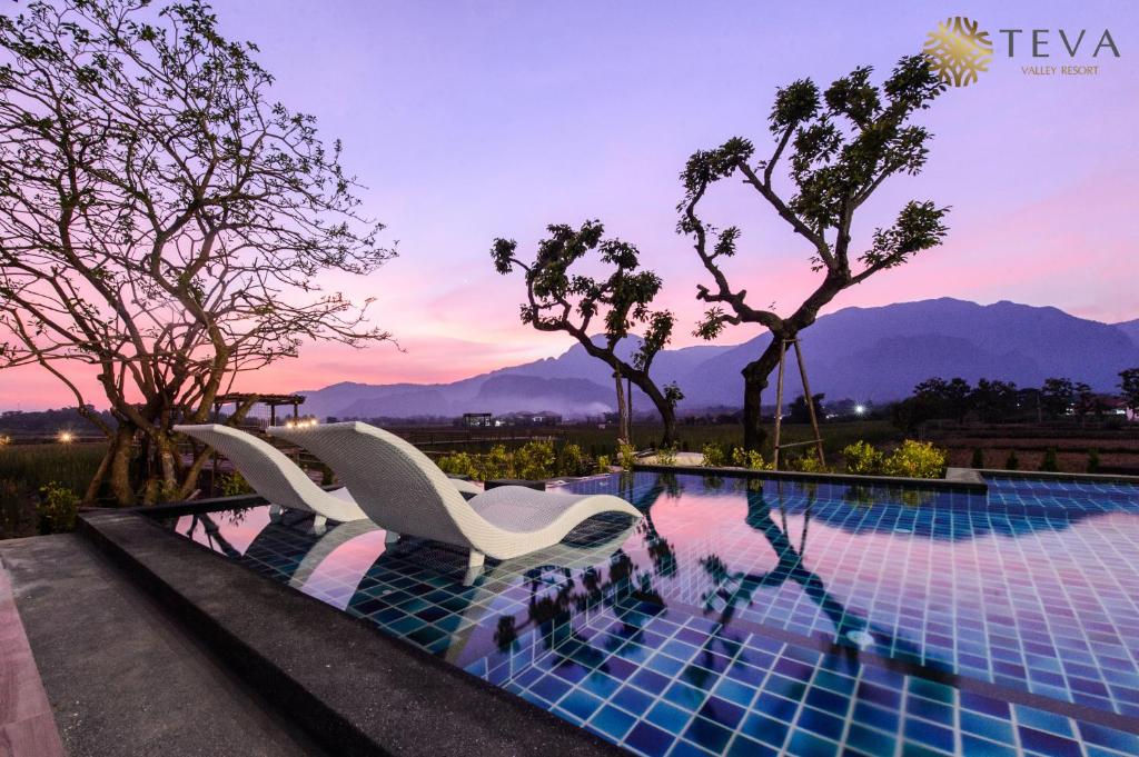 a resort pool with two white chairs and trees at TEVA Valley Resort in Chiang Rai