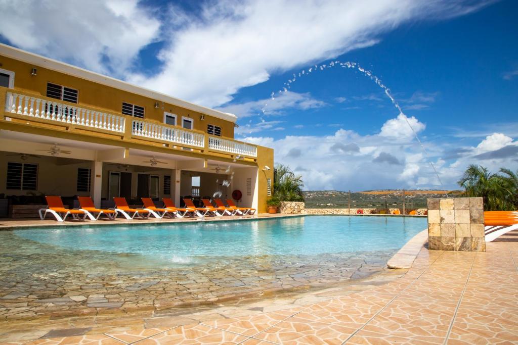 a swimming pool in front of a building with chairs at Hillside Resort Bonaire in Kralendijk