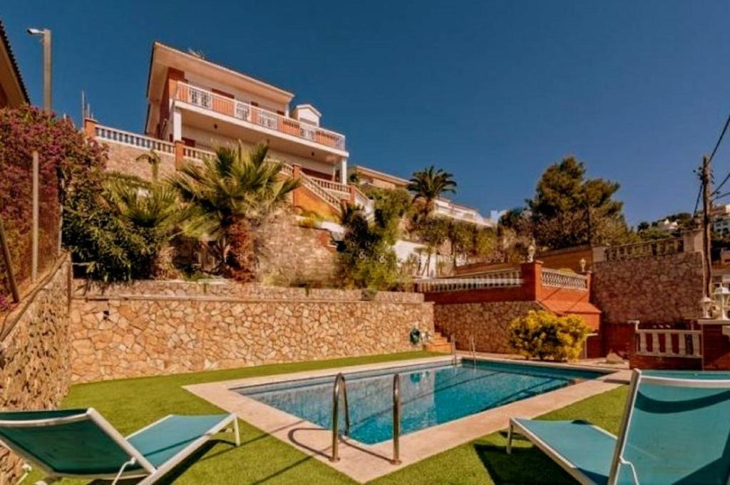 a swimming pool with two chairs and a building at Chalet Santa Susana in Santa Susanna