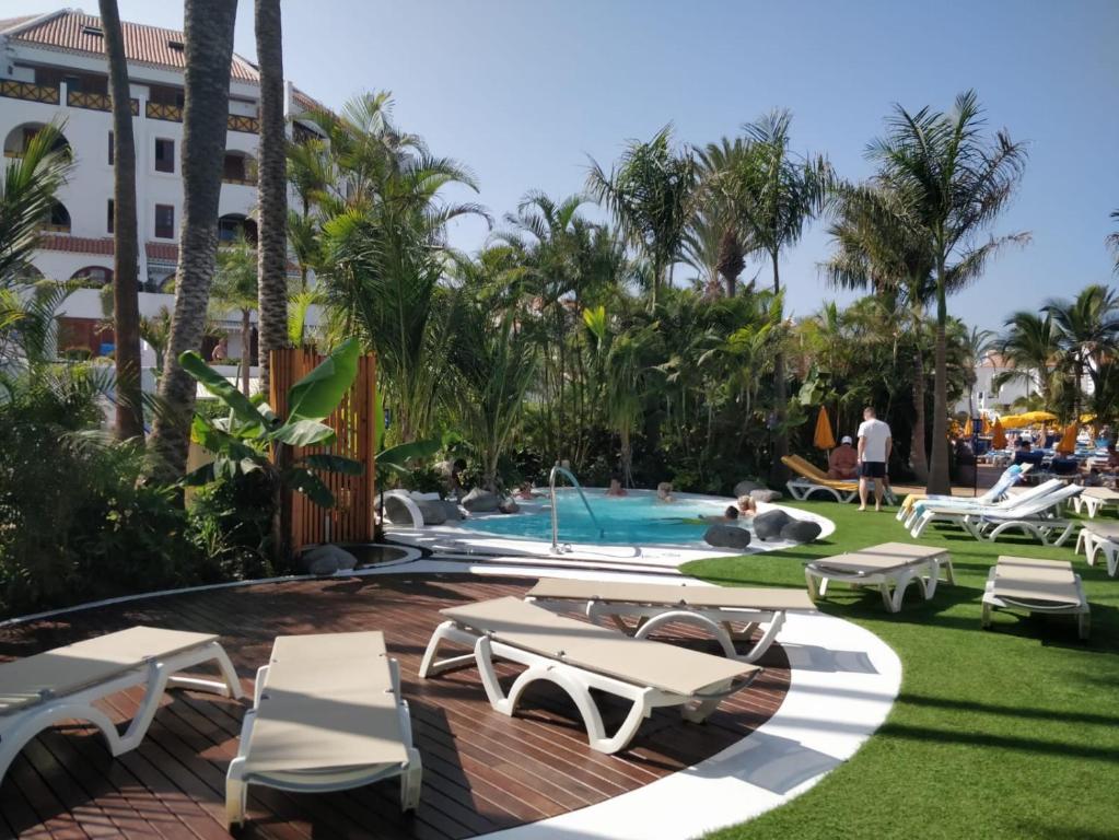 un complexe avec une piscine, des chaises longues et des palmiers dans l'établissement Seafront New Modern Apt, à Playa de las Americas