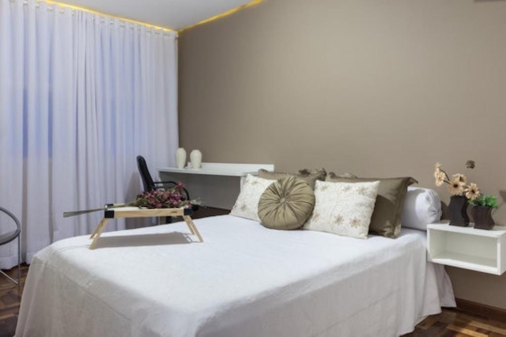 1 dormitorio con 1 cama blanca grande con silla en Pertinho CONSULADO AMERICANO Ar Condicionado 2 quartos Até 5 pessoas Av Carlos Gomes, en Porto Alegre