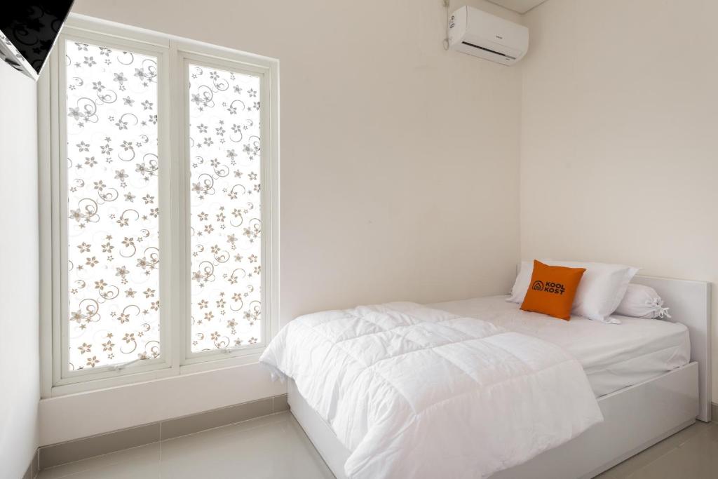 a white bedroom with a bed and a window at KoolKost near T2 Juanda Airport in Sidoarjo