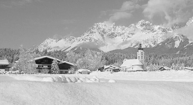 a black and white photo of a church with a snow covered mountain at APARTMENTS Pension Foidl in Oberndorf in Tirol