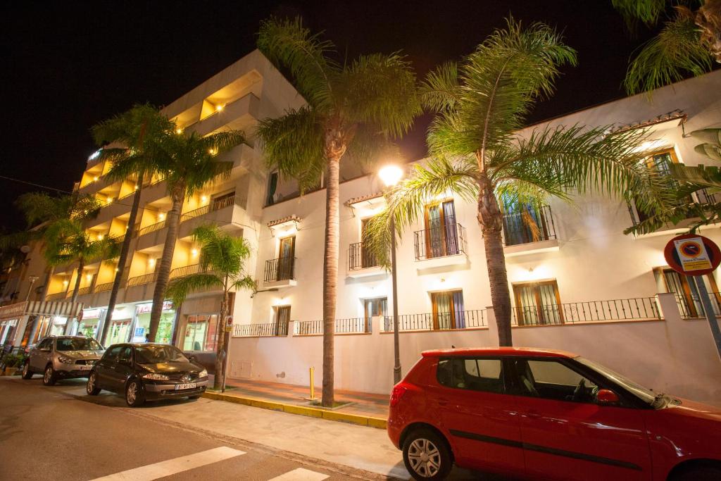 un coche rojo estacionado frente a un edificio con palmeras en Hotel Carmen Almuñécar, en Almuñécar