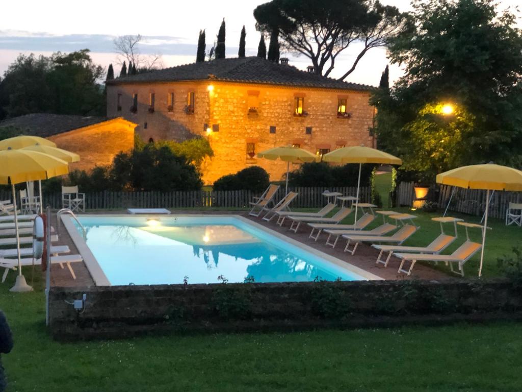 a pool with chairs and umbrellas in front of a building at villa San Fabiano with heated pool in Monteroni dʼArbia