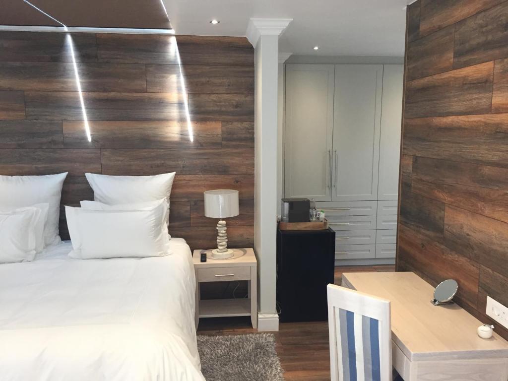 a bedroom with a white bed and a wooden wall at Gull on the Bay Boutique Guest House in Bloubergstrand