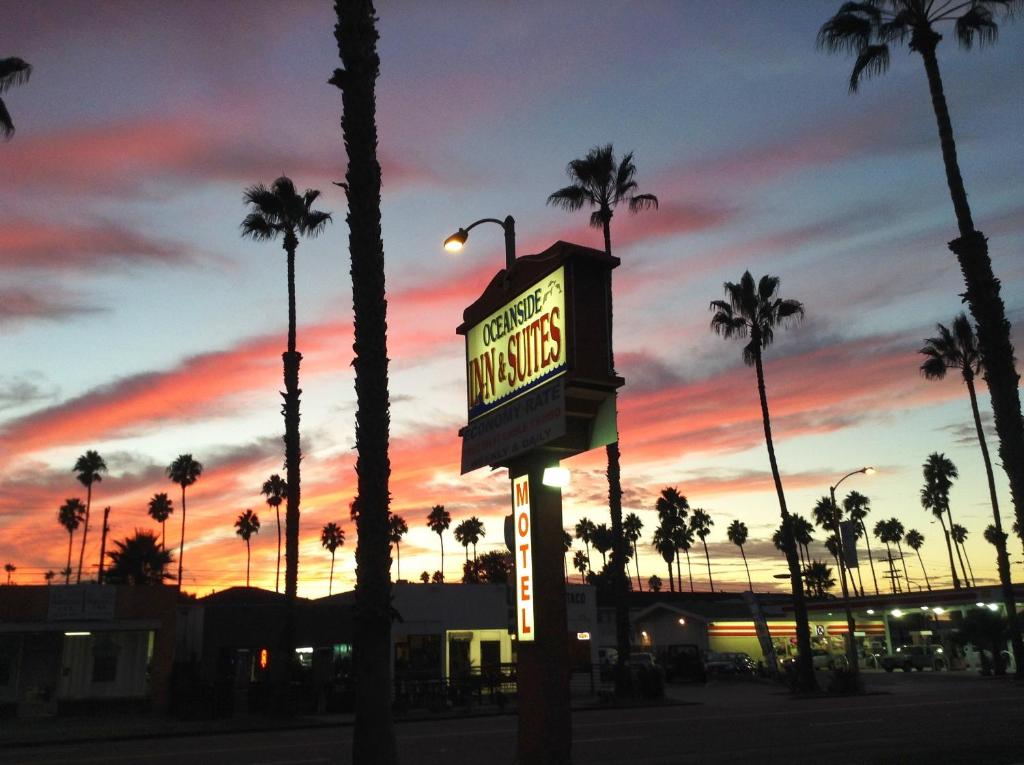 a neon sign in front of palm trees at sunset at Oceanside Inn and Suites in Oceanside