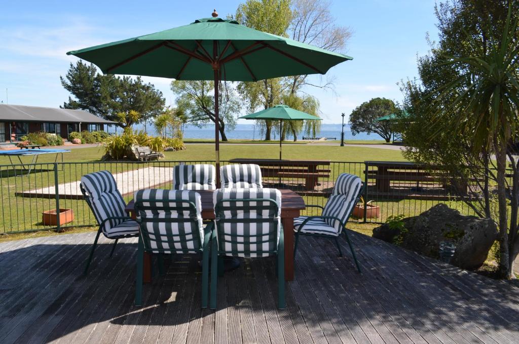 a table with chairs and a green umbrella at Cedarwood Lakeside Motel & Conference Venue in Rotorua