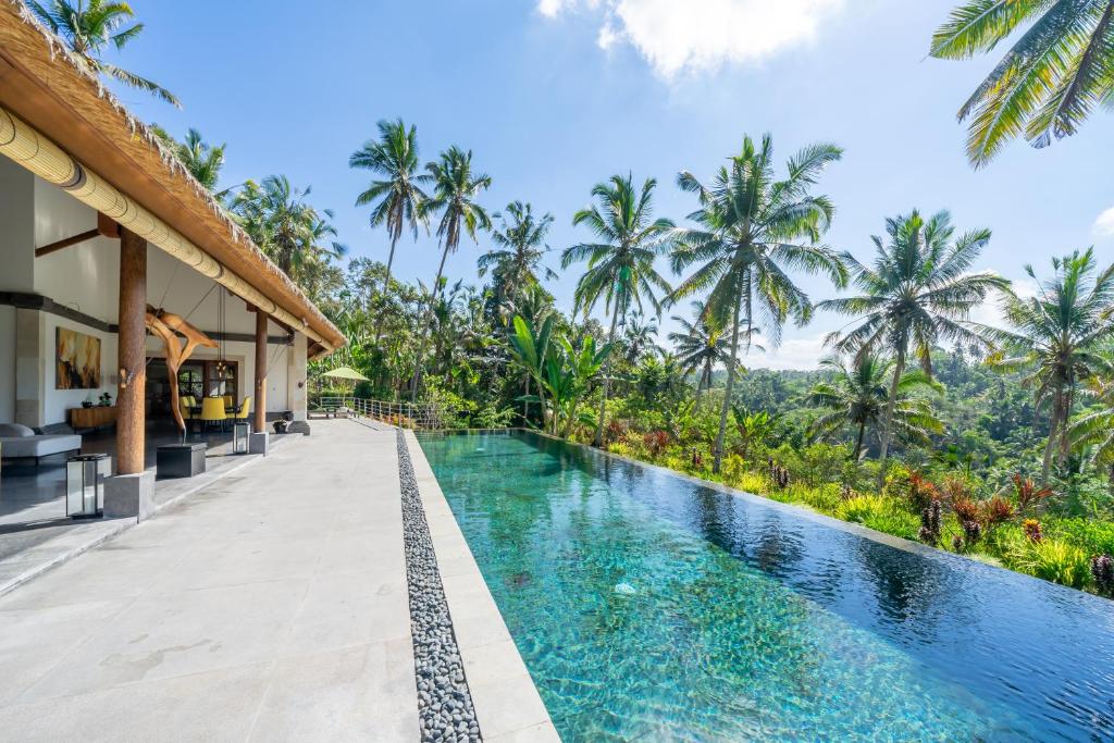 an infinity pool at a resort with palm trees in the background at Villa Themma Jungle - Sumptuous 3BR Luxury Villa with Majestic Jungle View North of Ubud in Ubud