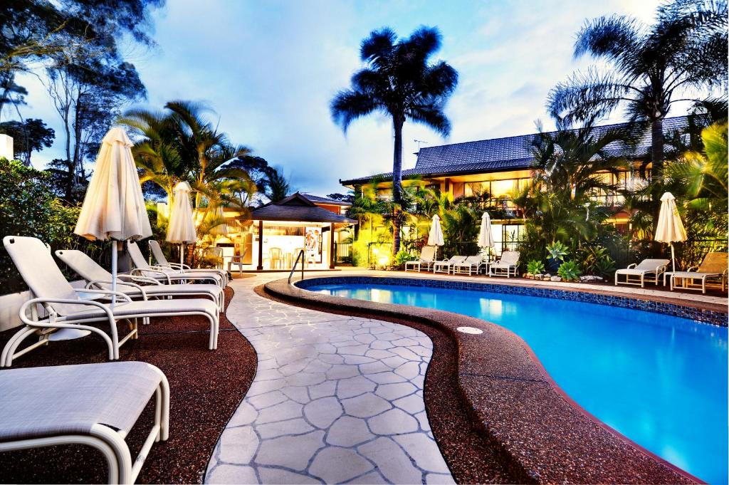 a swimming pool with chairs and tables in front of a large building at Smugglers On The Beach in Coffs Harbour