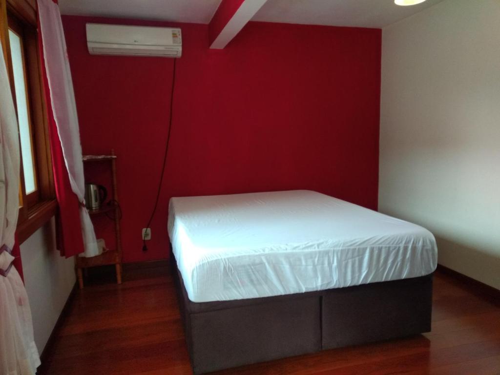 a small bedroom with a white bed in a red wall at QUARTO Jardim da Serra in Nova Petrópolis
