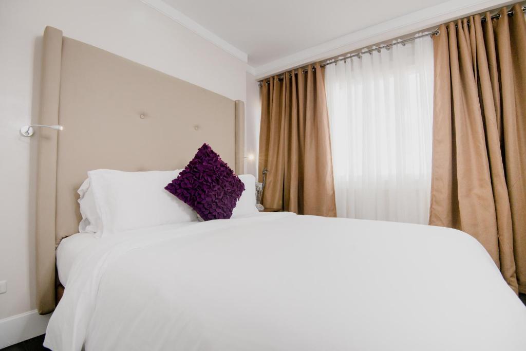 a white bed with purple pillows next to a window at Sta Barbara Residence Hotel in Cebu City