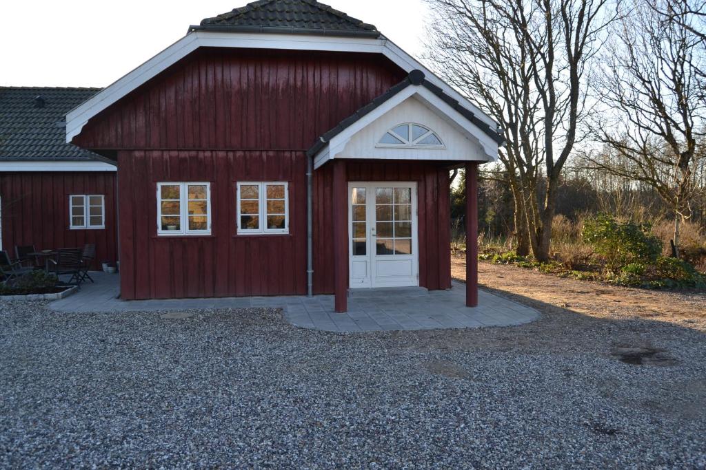 a red barn with a white door on a gravel driveway at Mosborg in Ulfborg