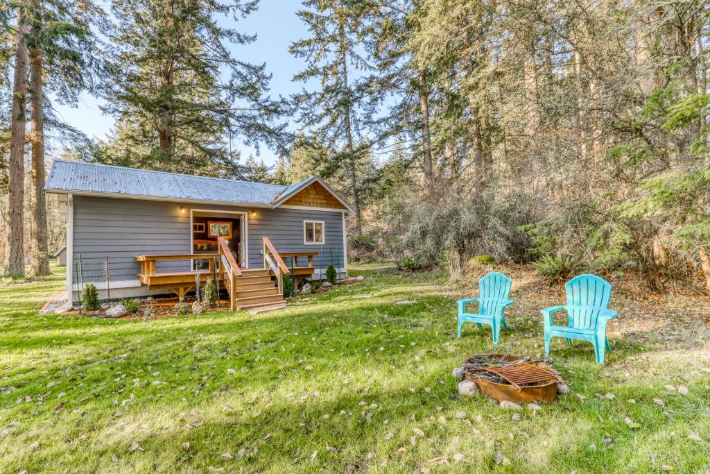 una cabaña en el bosque con dos sillas azules en el patio en Little House in the Big Woods en Freeland