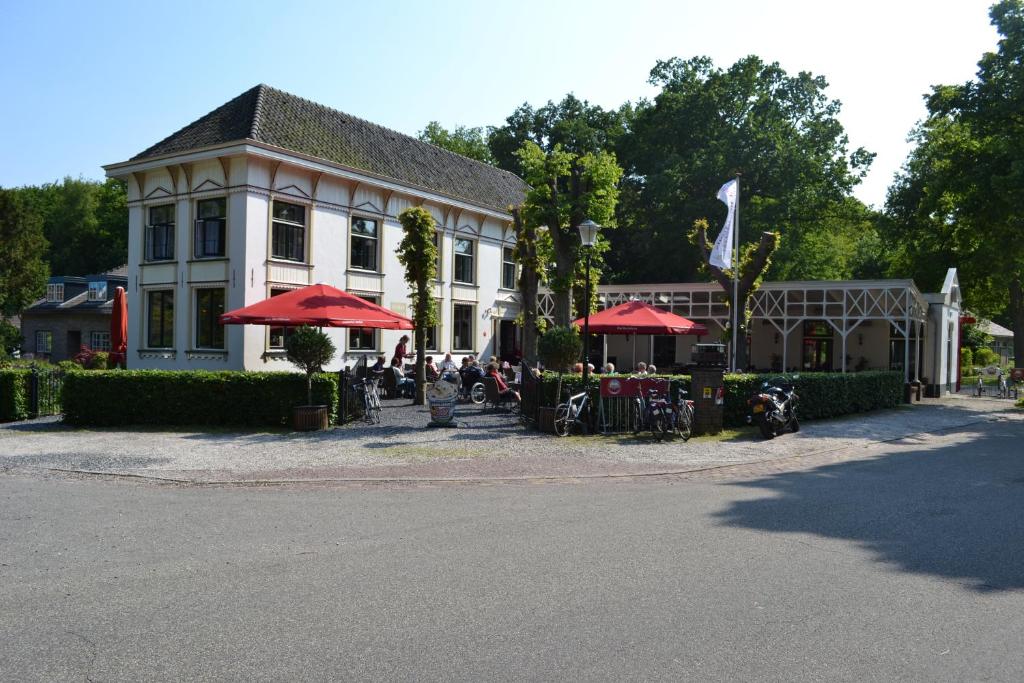 un bâtiment avec des tables et des parasols rouges devant lui dans l'établissement Hotel-Restaurant Het Rechthuis, à Muiderberg