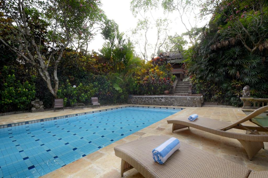 una piscina con 2 tumbonas junto a ella en Rumah Ganesha Ubud, en Ubud