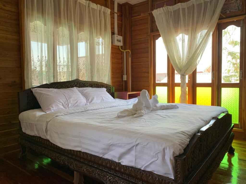 a bedroom with a bed with white sheets and windows at Sano Houes in Sukhothai