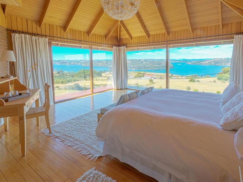 a bedroom with a bed and a desk and large windows at Hotel Boutique El Quinto in Castro