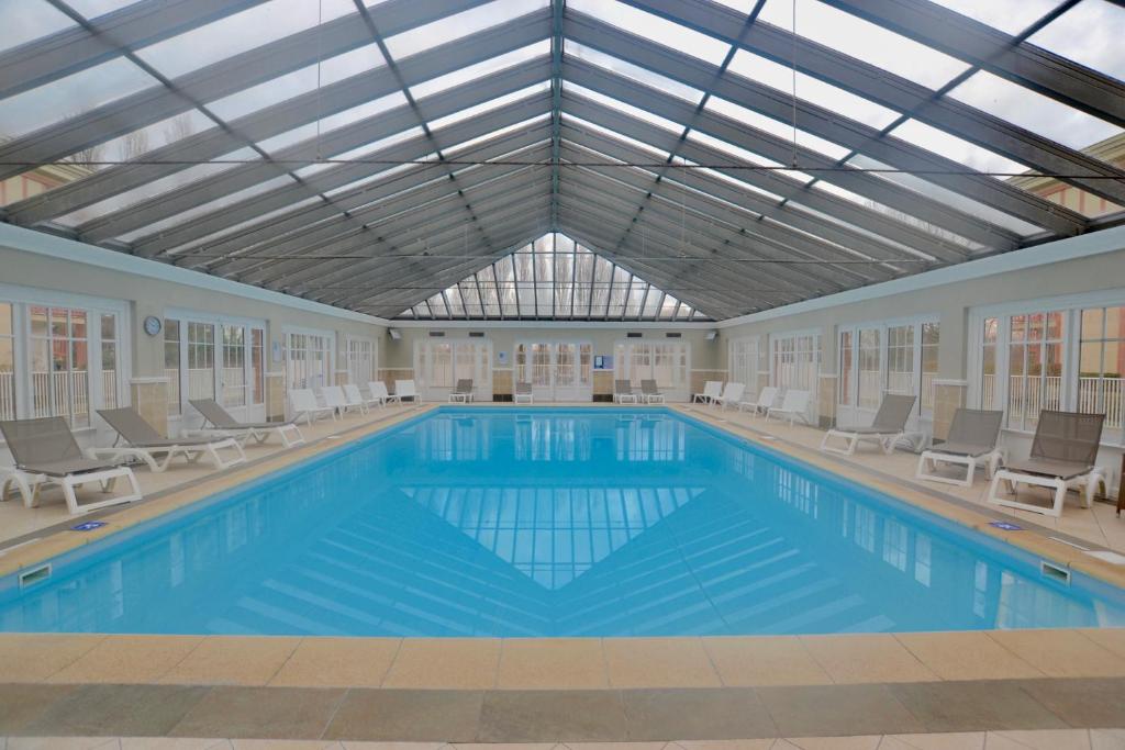 a large swimming pool with chairs and a ceiling at AC Tourisme Le Touquet - Appartements avec piscine et tennis in Le Touquet-Paris-Plage