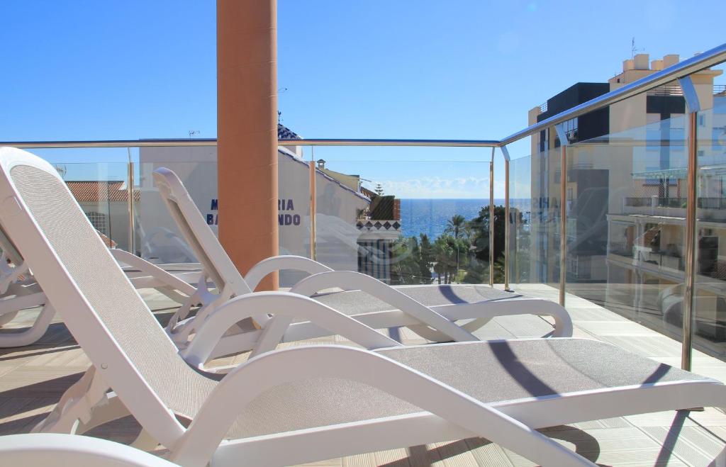 une rangée de chaises blanches assises sur un balcon dans l'établissement Apartamentos Guerrero, à Torre del Mar