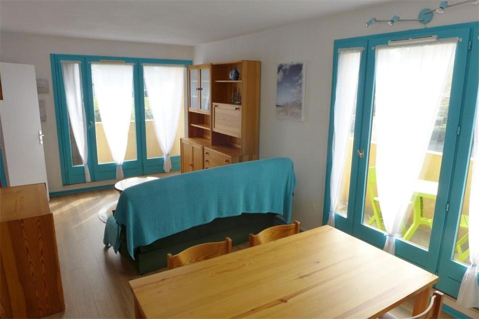 a living room with a wooden table and windows at Réf 546, Seignosse océan , Appartement classé 2 étoiles , plage et centre à 5mn, 5 personnes in Seignosse