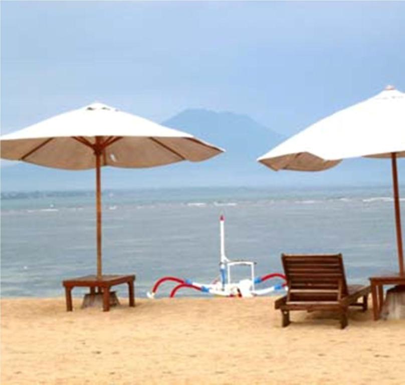 two chairs and two umbrellas on a beach at Gazebo Beach Hotel in Sanur