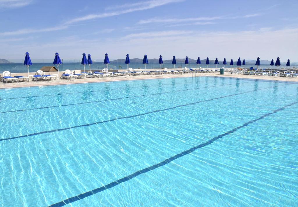 a large swimming pool next to a beach with umbrellas at Mastichari Bay Hotel in Mastihari