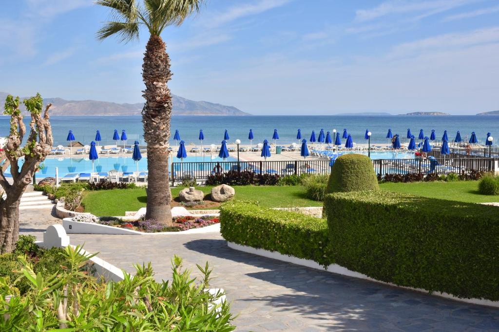 a resort with a palm tree and a beach with blue umbrellas at Mastichari Bay Hotel in Mastichari