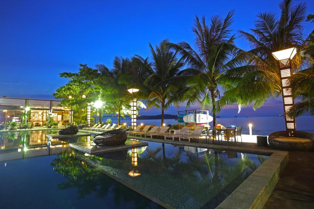 a resort pool with palm trees and chairs at night at Queenco Hotel & Casino in Sihanoukville
