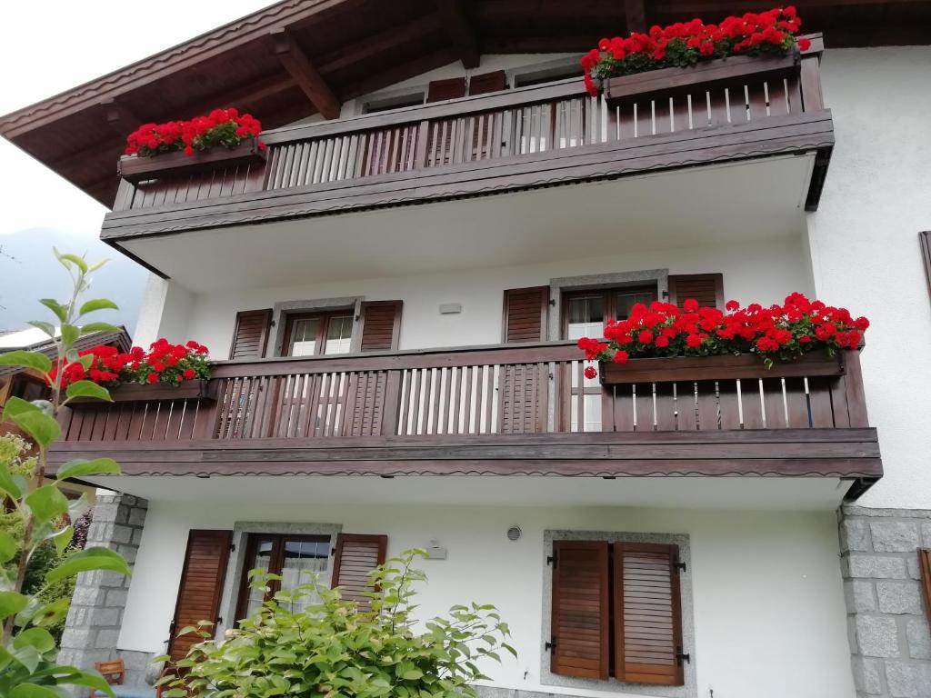 a white house with red flowers on balconies at Appartamento con giardino in Carisolo