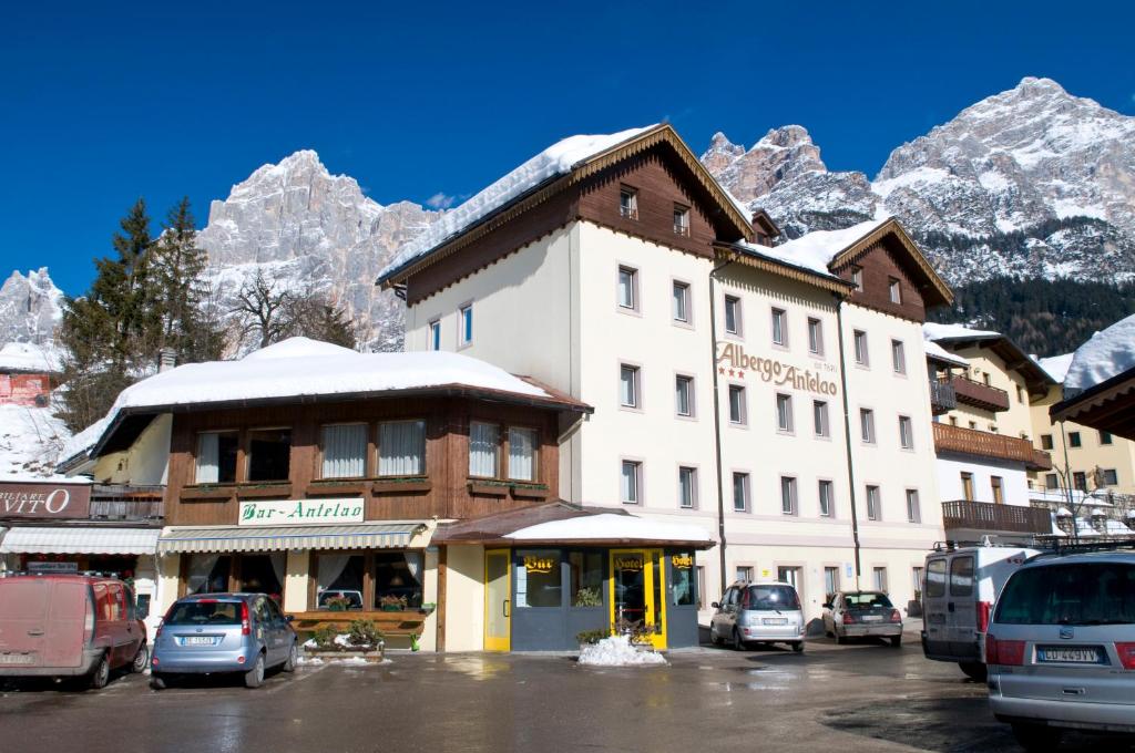 a hotel with cars parked in a parking lot with mountains at Albergo Antelao in San Vito di Cadore